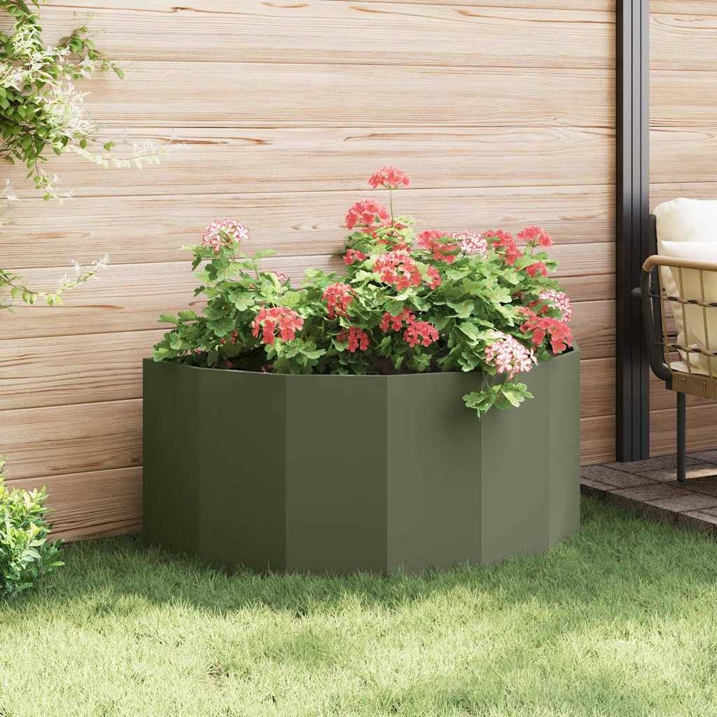 Ein runder grüner Pflanzentopf, gefüllt mit blühenden roten und rosa Blumen, steht auf einer Terrasse mit einer Holzwand im Hintergrund.