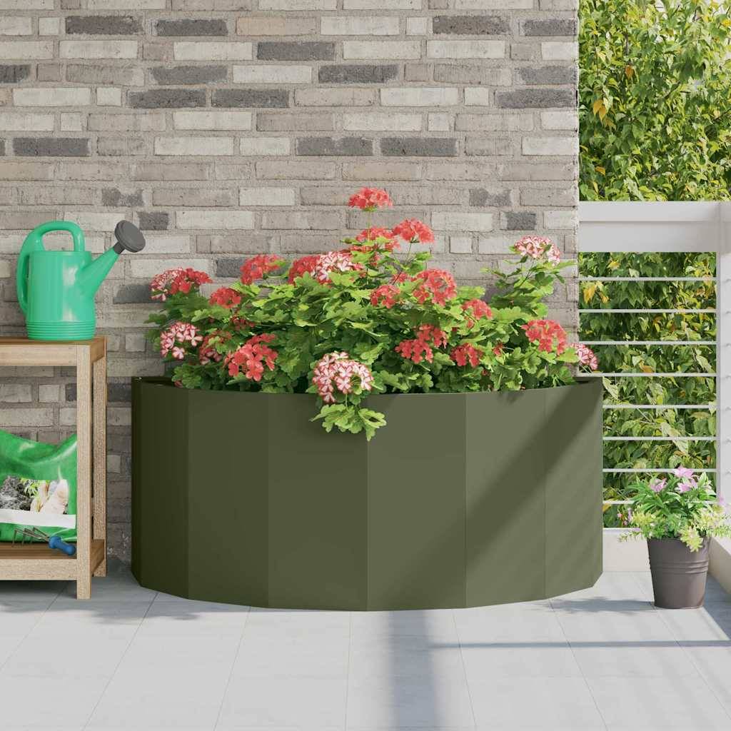 Ein grüner Pflanzkübel gefüllt mit blühenden roten und pinken Blumen auf einer sonnigen Terrasse, mit einer Gießkanne und einer kleinen Topfpflanze in der Nähe.