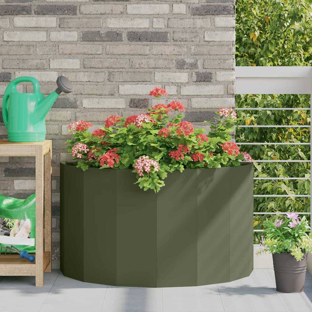 Ein grüner Blumentopf mit rosa und roten Blumen auf einem Balkon. Eine Gießkanne steht auf einem Holzregal in der Nähe.