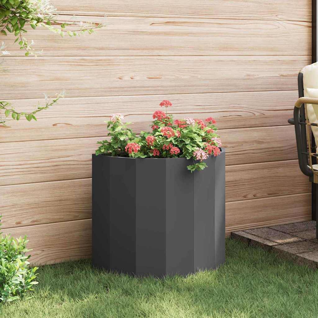 Ein schwarzer Pflanzkübel mit rosa und weißen Blumen steht auf einem Rasengrund neben einer Holzwand und verleiht der Gartenumgebung eine Prise Farbe.