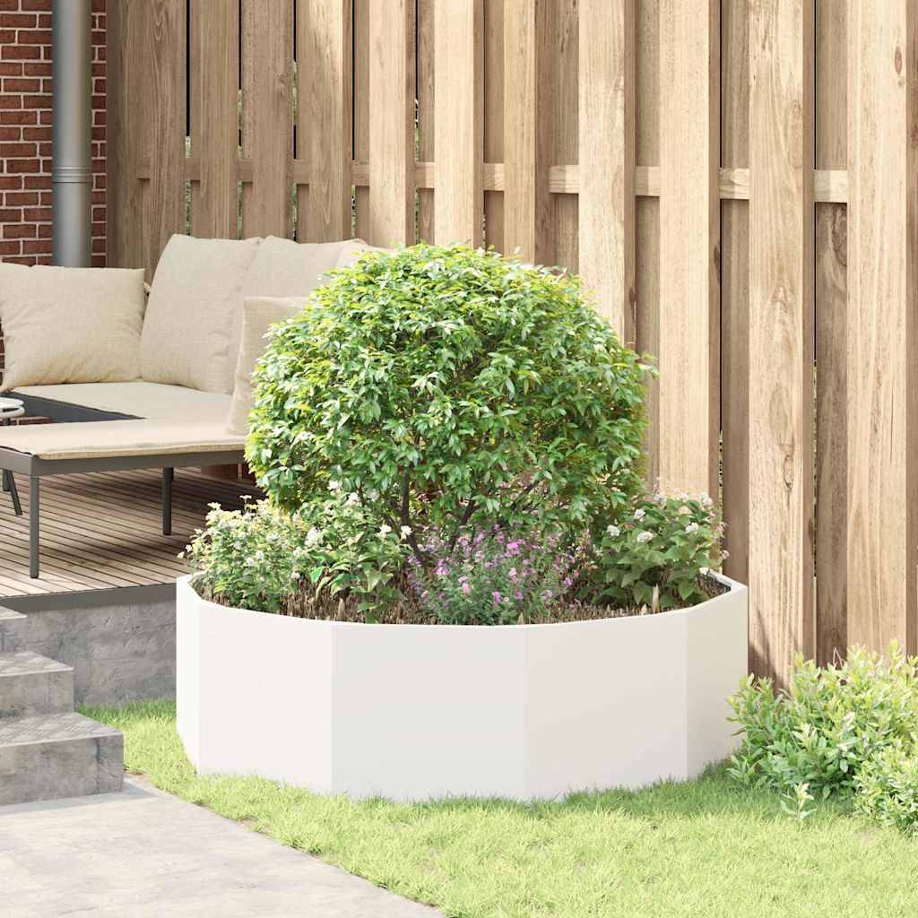 Ein kleiner, runder Strauch in einem weißen Pflanzgefäß steht auf einer Terrasse mit Holzzaun und einem Ecksofa und schafft einen ruhigen Außenbereich.