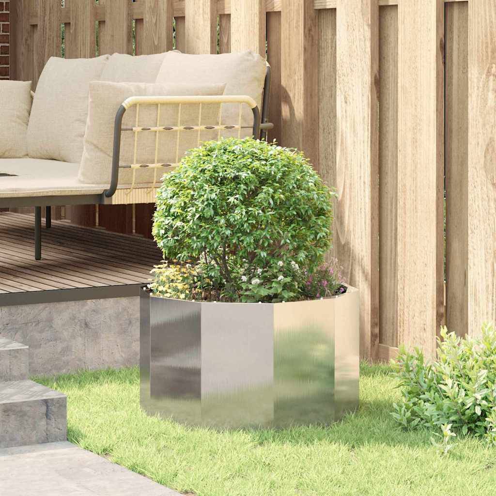 Eine gemütliche Sitzecke im Freien mit einem gepolsterten Sofa und einem runden, grünen Strauch in einem glänzenden Metallübertopf auf einer Rasenterrasse.