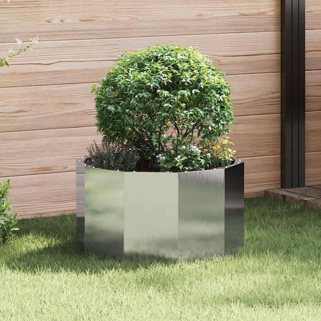 Ein glänzender metallischer Pflanzentopf in einem Garten enthält einen üppig grünen Busch und kleine Blumen, vor einem Holzvertäfelungshintergrund.