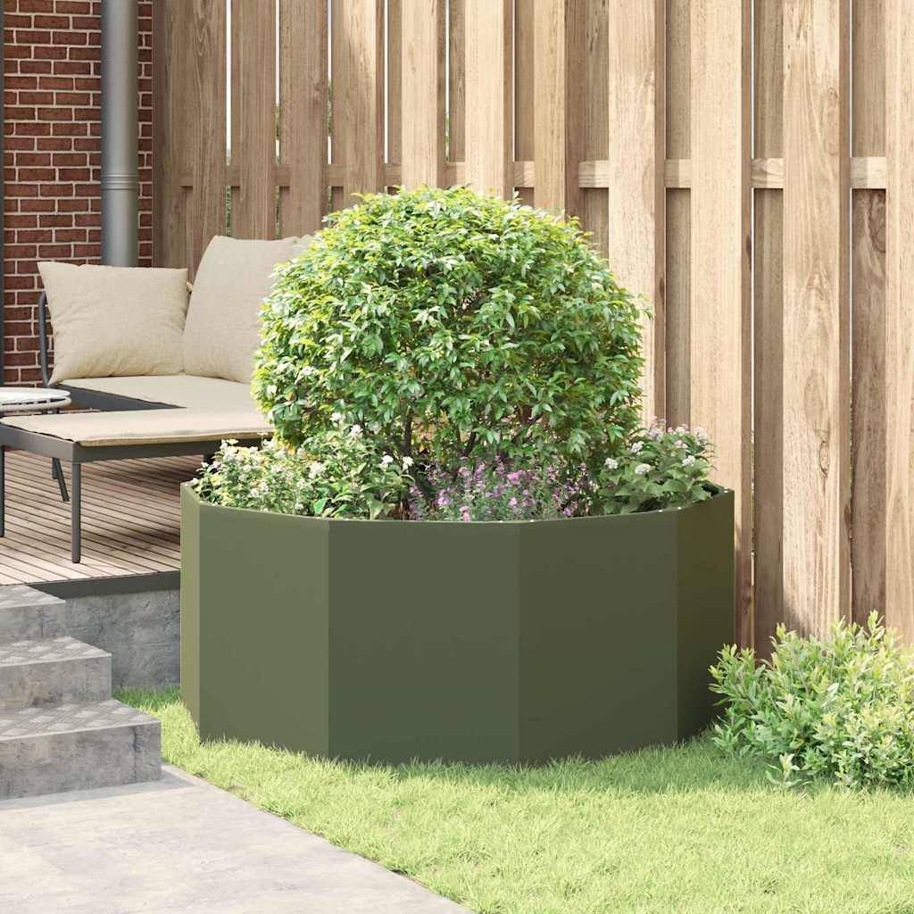 Ein grüner Busch in einem sechseckigen Pflanzkübel steht auf einer Terrasse neben einer Treppe. Ein gepolstertes Outdoor-Sofa sitzt in der Nähe an einem Holzzaun.