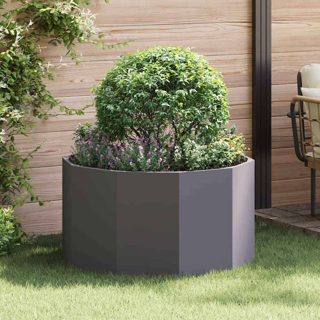 Ein runder Pflanzkübel mit einem üppigen grünen Strauch und lila Blüten, der auf einer Holzterrasse vor einer Holzwand und einem Metallpfeiler steht.
