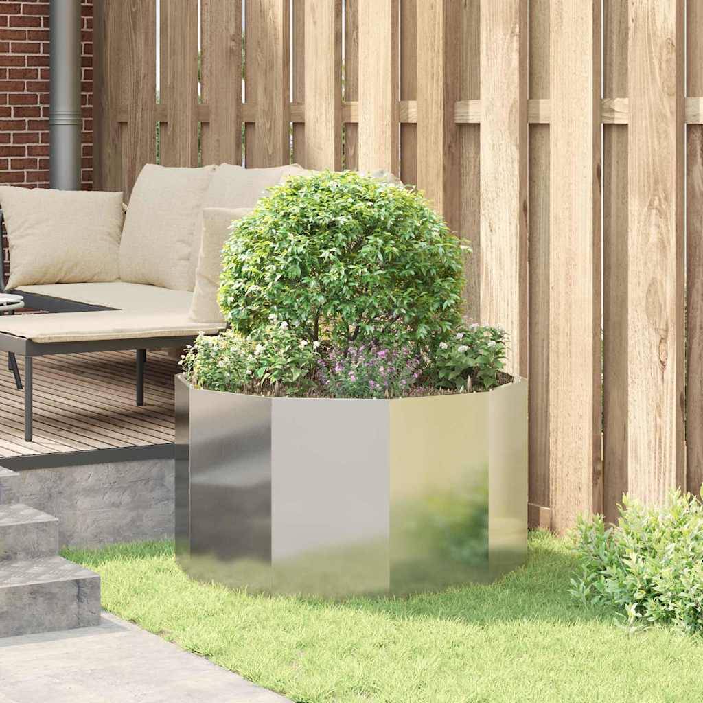 Eine Terrasse mit einem weißen Ecksofa und einem gepflegten grünen Strauch in einem modernen, reflektierenden Pflanzgefäß. Holzzaun im Hintergrund.