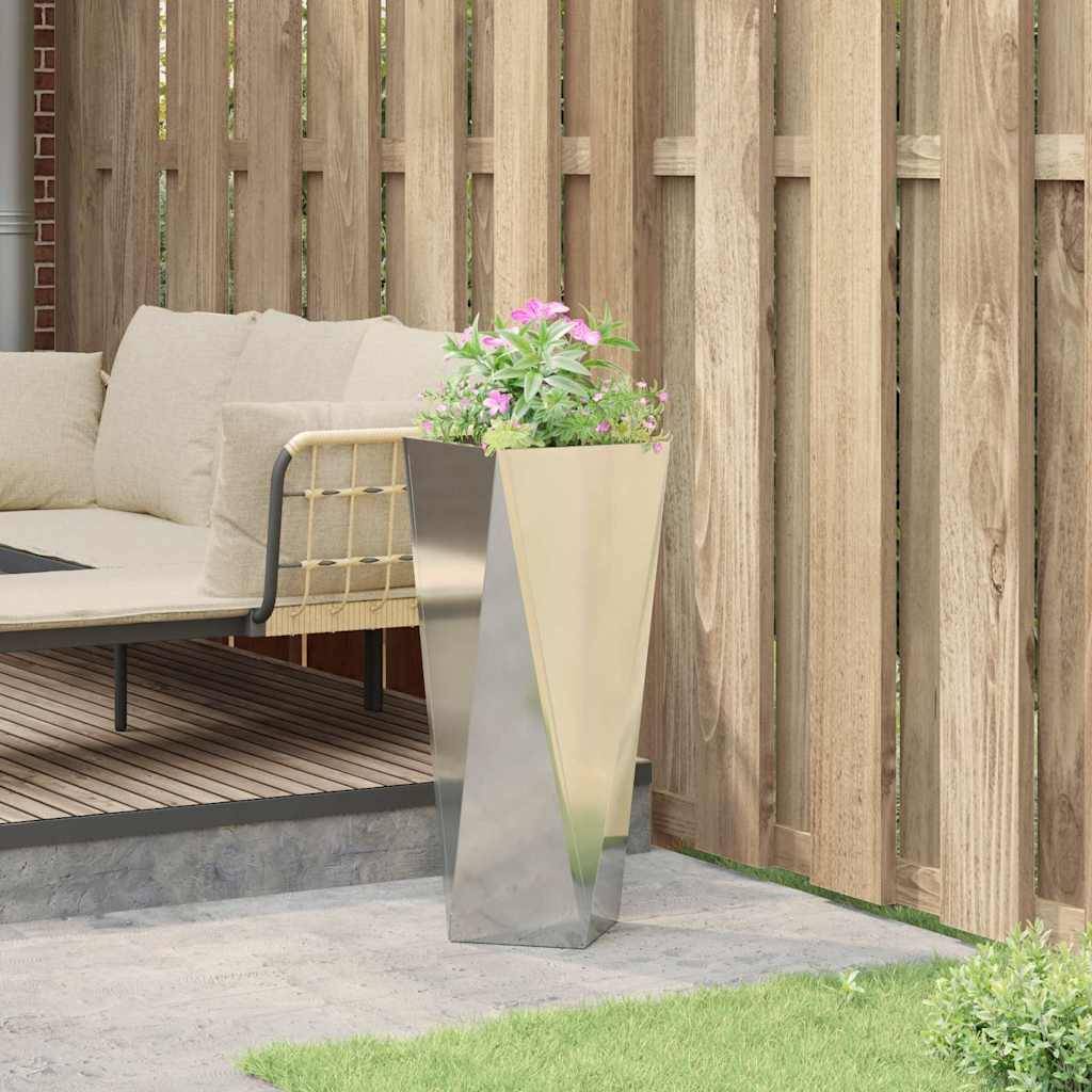 Eine Terrasse zeigt ein beiges L-förmiges Sofa mit weißen Kissen, das vor einem Holzzaun steht. Ein hoher metallischer Pflanzenkübel beherbergt eine blühende Pflanze.