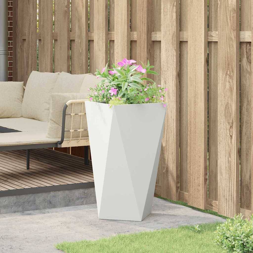 Eine Terrassenanlage mit einem beigen Outdoor-Sofa auf einer Holzterrasse, neben einem großen weißen geometrischen Pflanzgefäß mit rosa Blumen, umgeben von einem Holzzaun.