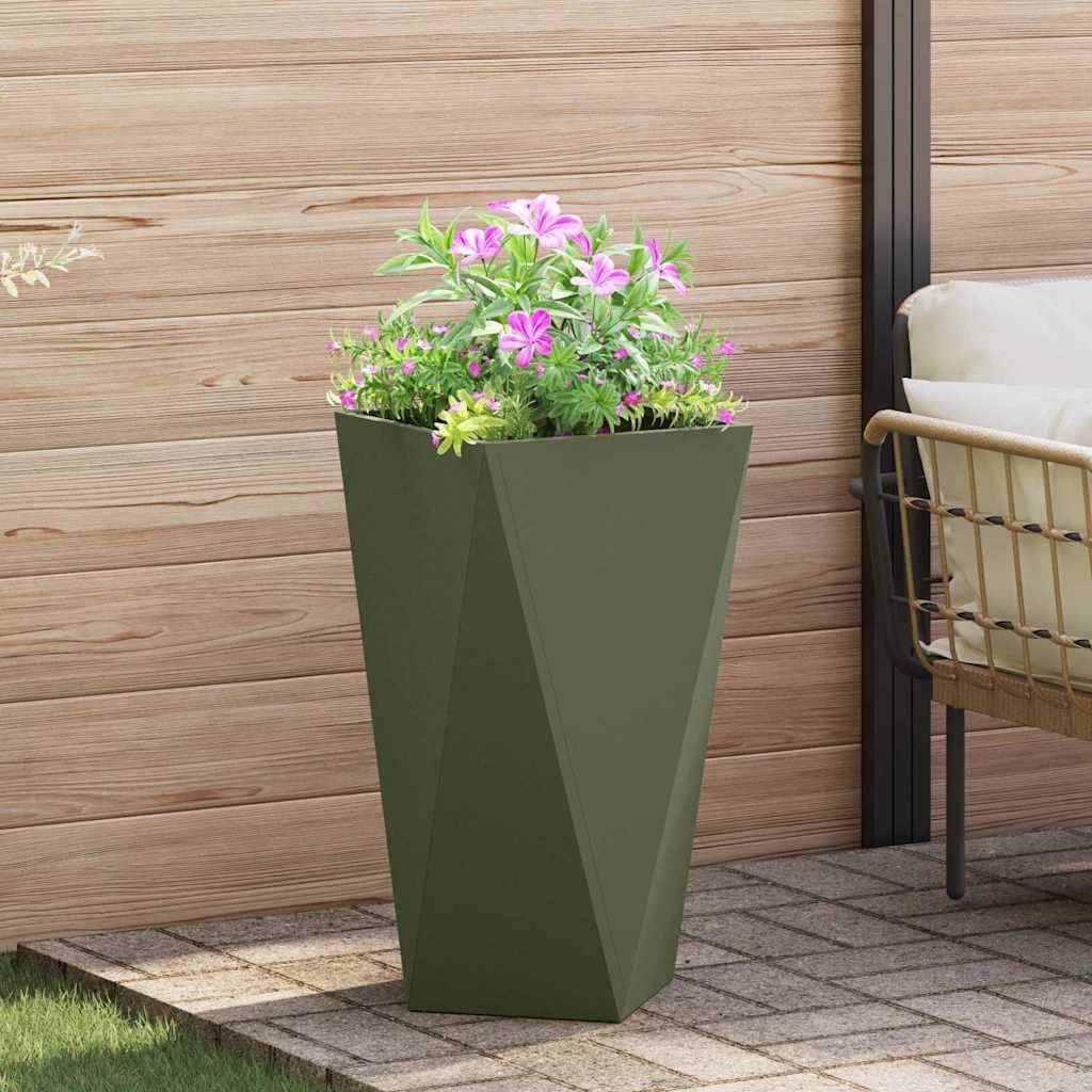 Ein hoher, moderner grüner Blumentopf, gefüllt mit rosa und weißen Blumen, steht auf einer Terrasse mit Holzvertäfelung und einem Rattan-Stuhl in der Nähe.
