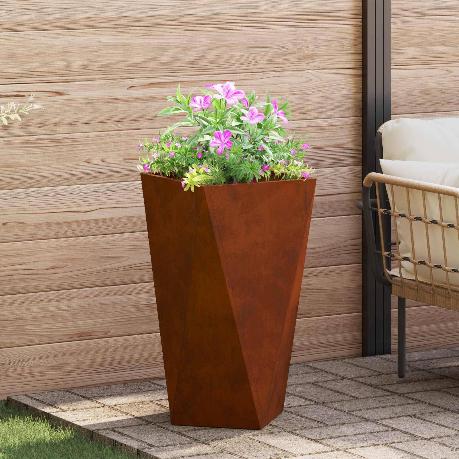 Ein großes, rostfarbenes Pflanzgefäß mit rosa und weißen Blumen steht auf einer Terrasse neben einer hölzernen Wand und einem Außensitzbereich.