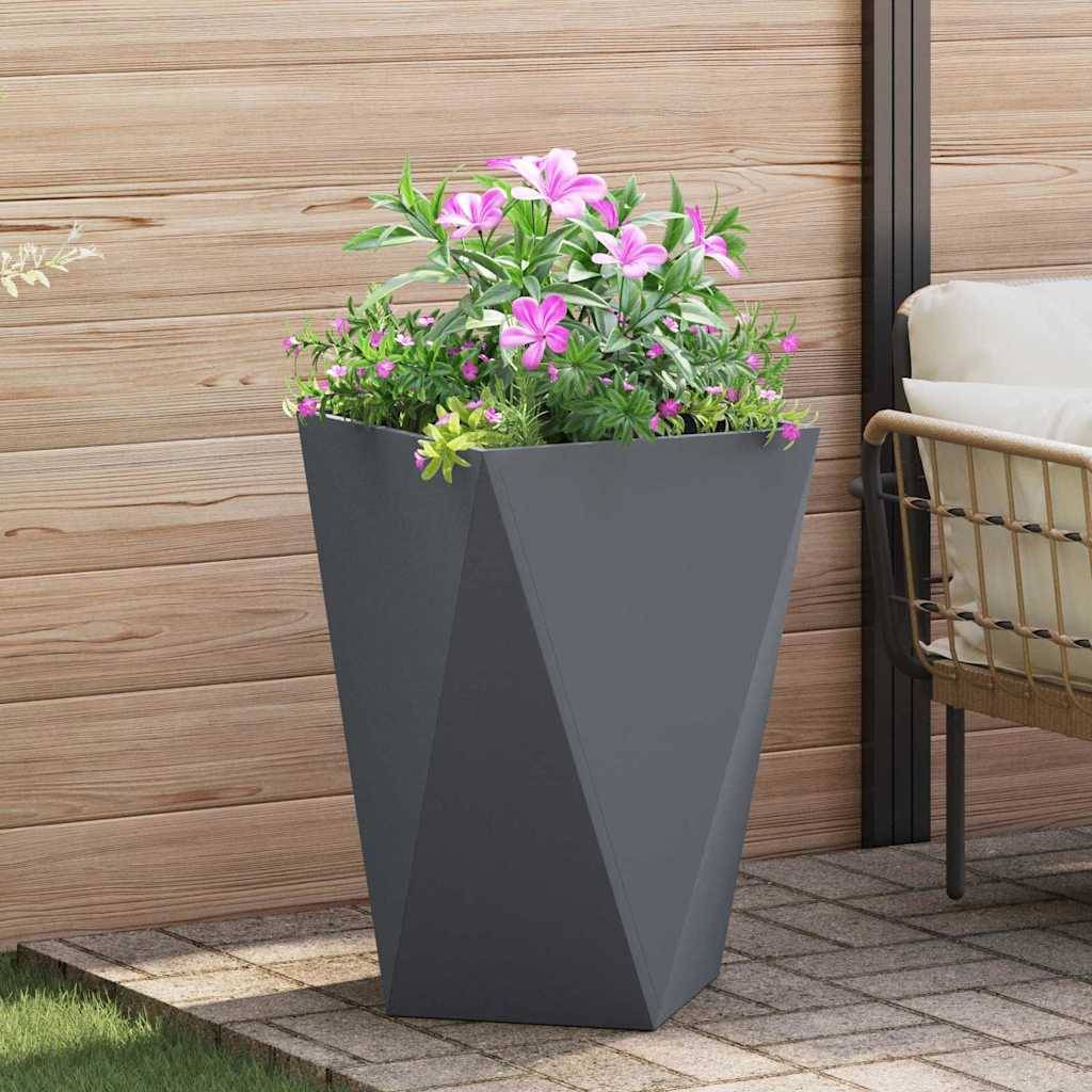 Ein schwarzer geometrischer Blumentopf mit blühenden rosa und weißen Blumen steht auf einer Terrasse mit hellholzfarbenen Wänden, neben einem Korbstuhl.