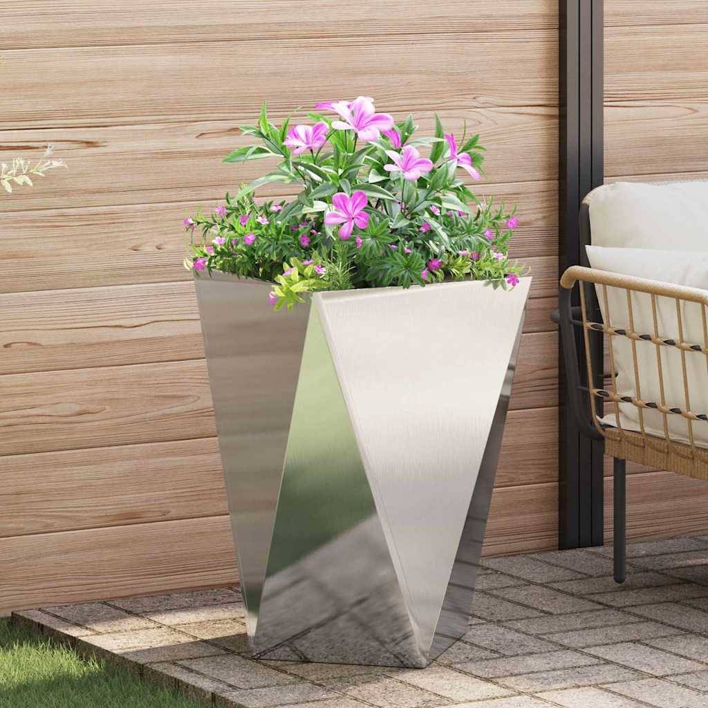 Ein moderner Metallpflanzer mit rosa Blumen auf einer gefliesten Terrasse neben einem Korbstuhl und einer Holzwand, der eine zeitgemäße Outdoor-Umgebung schafft.
