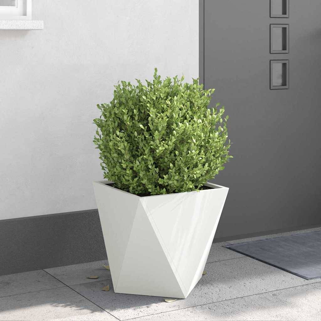 Ein geometrischer weißer Pflanzkübel mit einem belaubten grünen Strauch steht auf einer modernen Terrasse mit grauen Fliesen und einer grauen Wand im Hintergrund.