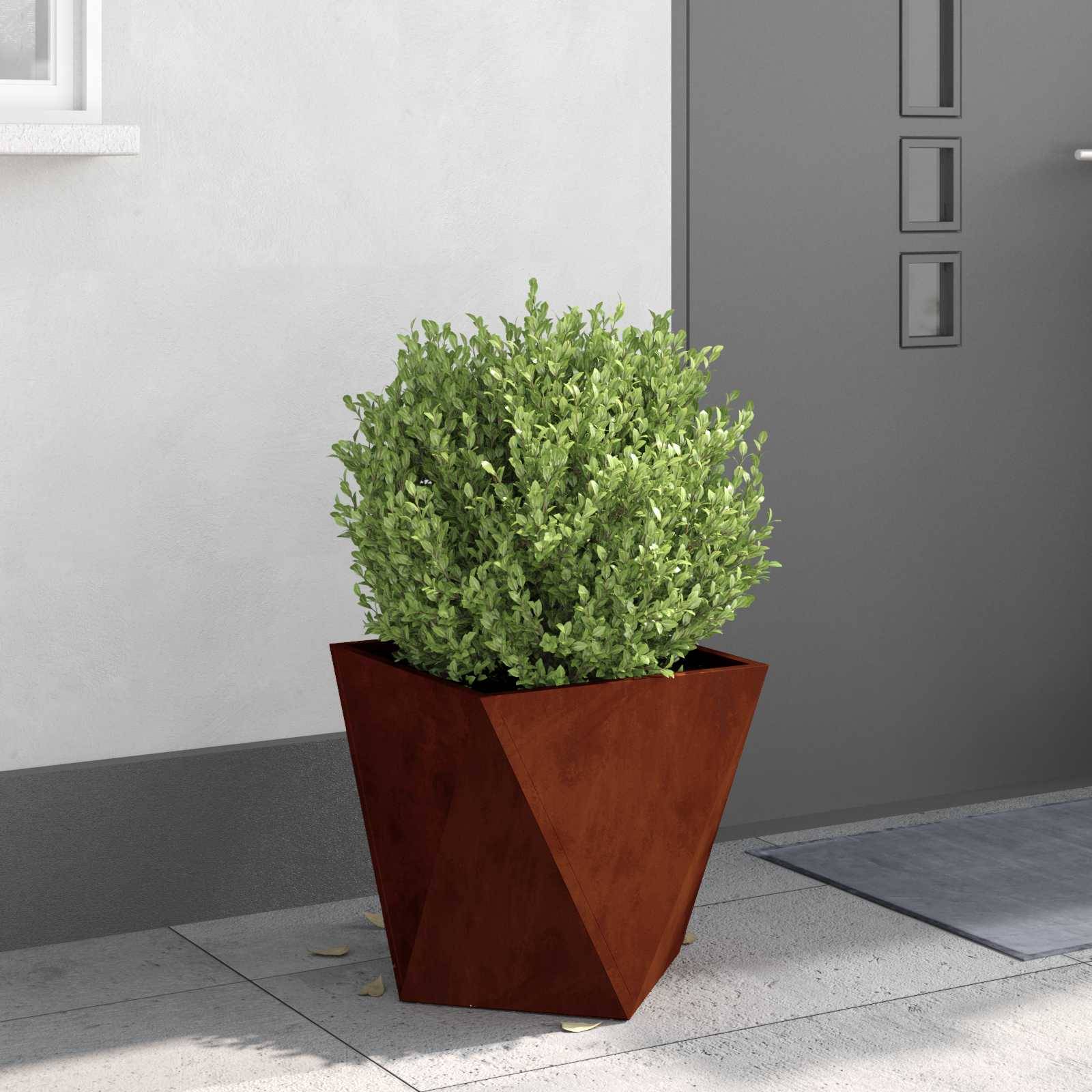 Ein kleiner grüner Strauch in einem rostfarbenen, geometrischen Blumentopf steht auf einer grauen Terrasse in der Nähe einer modernen grauen Tür.