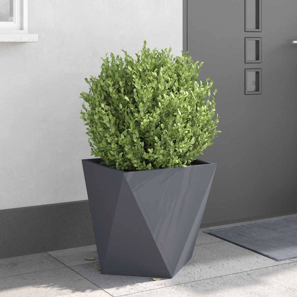 Ein geometrischer grauer Pflanzkübel beherbergt einen üppig grünen Strauch, der auf einer gepflasterten Terrasse neben einer grauen Gebäudefassade platziert ist und modernes Dekor andeutet.