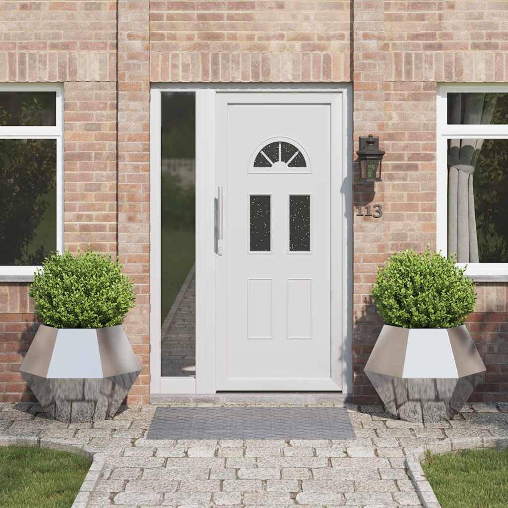 Eine weiße Haustür mit drei kleinen Fenstern wird von zwei großen Kübelpflanzen an einer Ziegelsteinfassade flankiert. Eine Hausnummer '113' ist sichtbar.