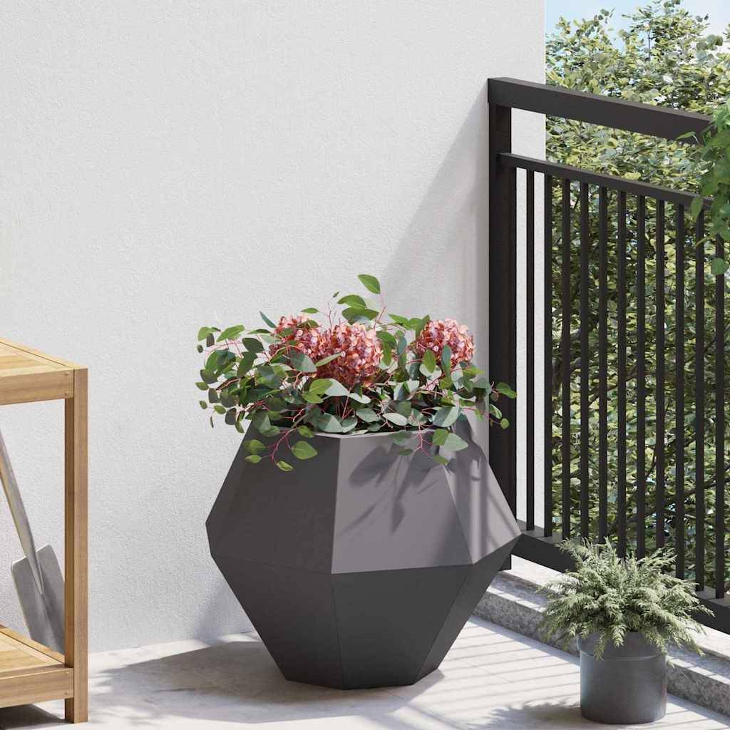 Ein sechseckiger Pflanzkübel mit rosa Blumen und grünen Blättern steht auf einer Terrasse neben einem schwarzen Metallgeländer. Ein Holzregal ist teilweise links zu sehen.