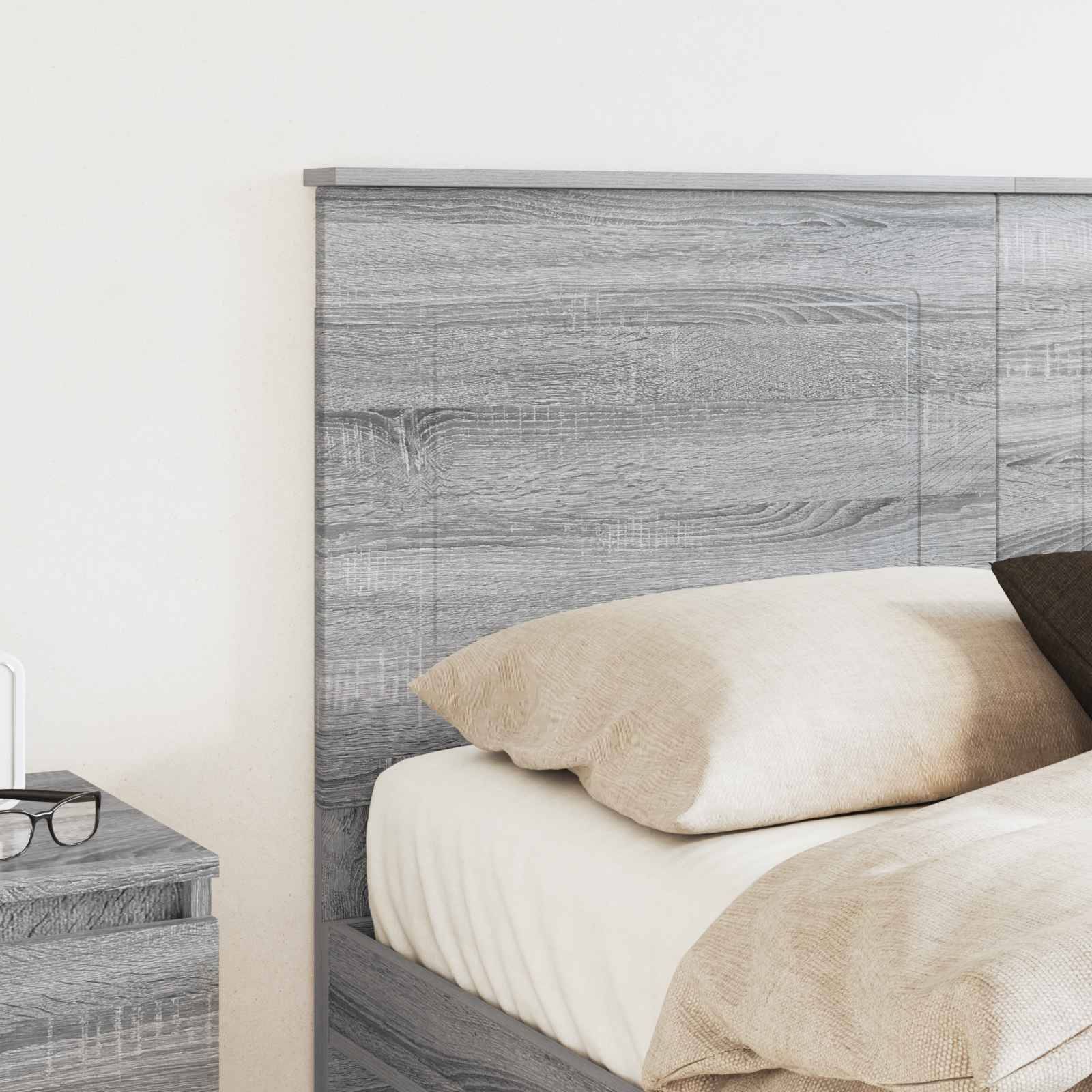Ein modernes Schlafzimmer mit einem grauen, holzstrukturierten Bettgestell, beigefarbener Bettwäsche und einem passenden Nachttisch, auf dem ein Smartphone aufgeladen wird.