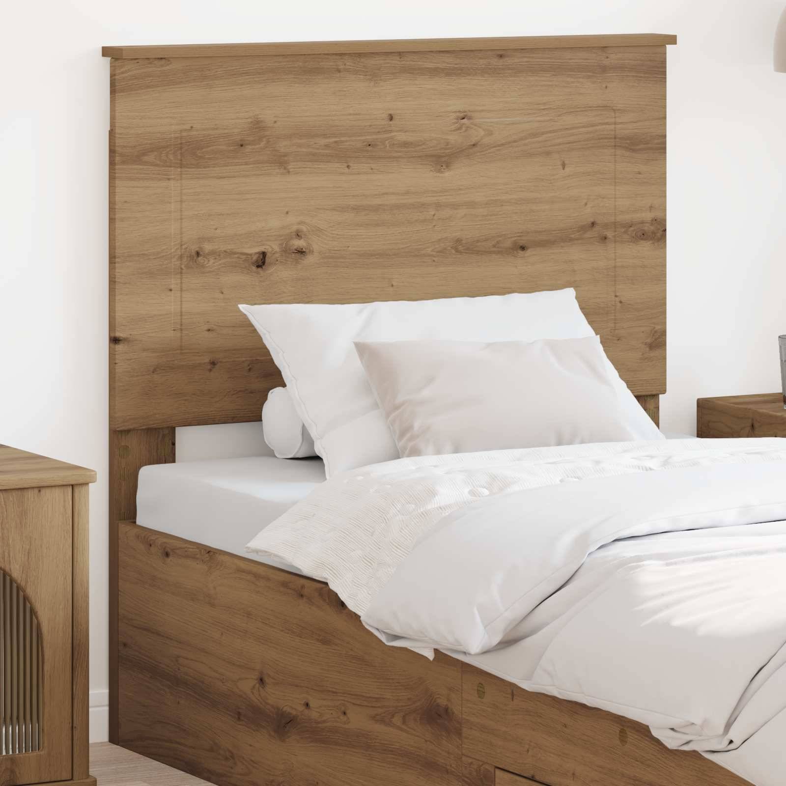 Ein ordentlich gemachtes Bett mit Holzkopfteil, weißen Kissen und einer weißen Decke neben einem hölzernen Nachttisch. Das Zimmer hat einen minimalistischen Stil.