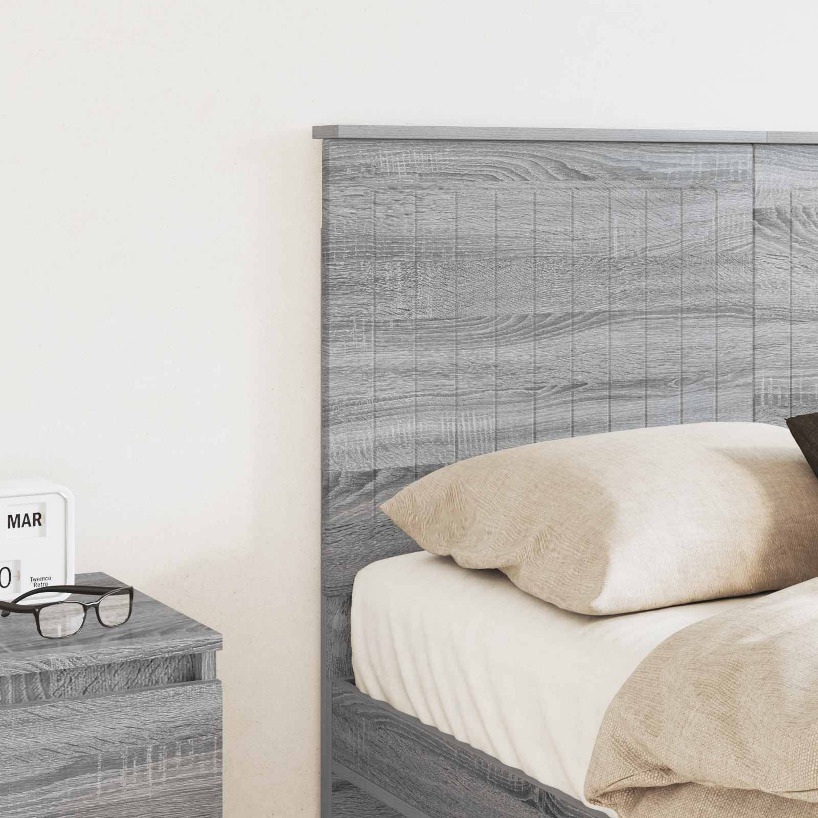 Ein Schlafzimmerszenario zeigt ein graues Holzbett mit beigen Kissen und einem passenden Nachttisch. Ein kleiner Kalender auf dem Tisch zeigt 