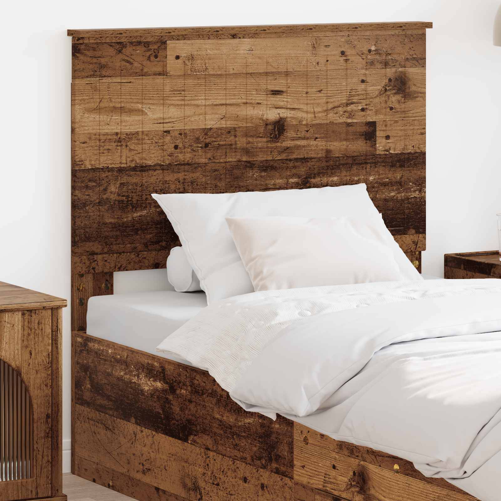 Ein rustikales Holzbett mit weißen Kissen und Laken steht neben einem passenden Holznachttisch in einem hellen Schlafzimmer.