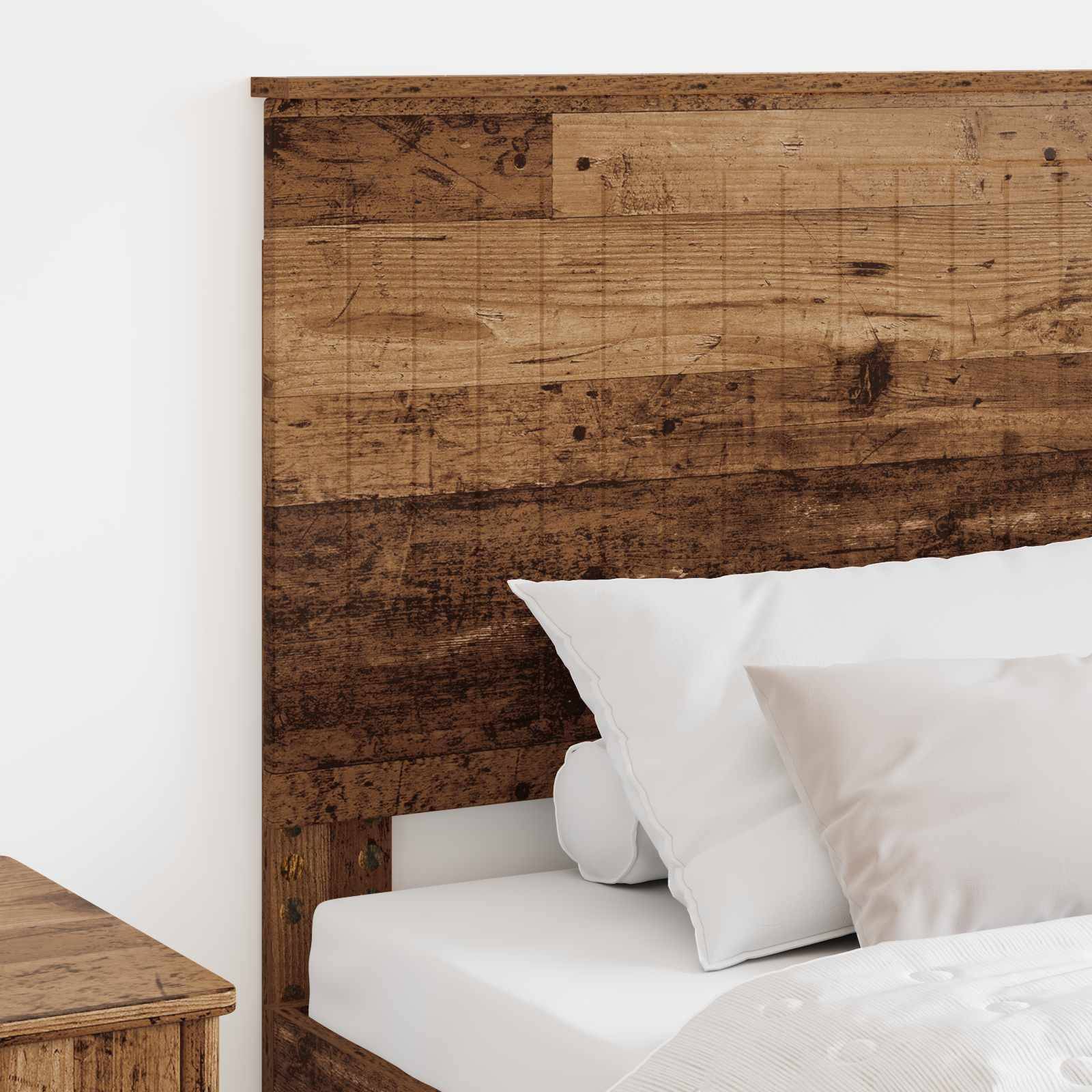 Ein rustikales Holzkopfteil mit einer leicht abgenutzten Textur, kombiniert mit einem weißen Bettkissen, vor einer hellfarbigen Wand.