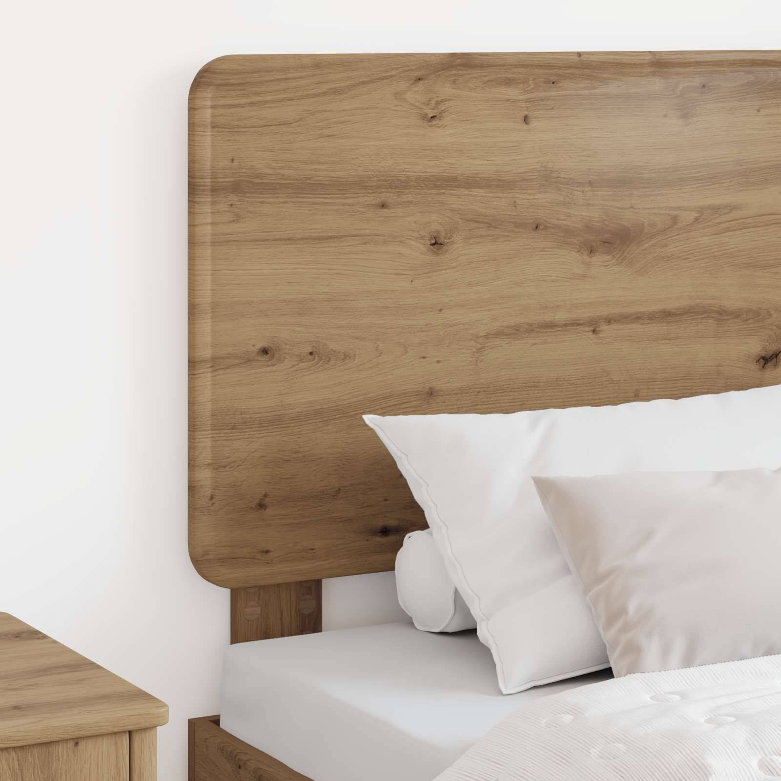 Holzbett mit Kopfteil, weißen Kissen und Bettdecke. Ein Teil eines hölzernen Nachttisches ist sichtbar. Einfaches, modernes Schlafzimmereinrichtung.