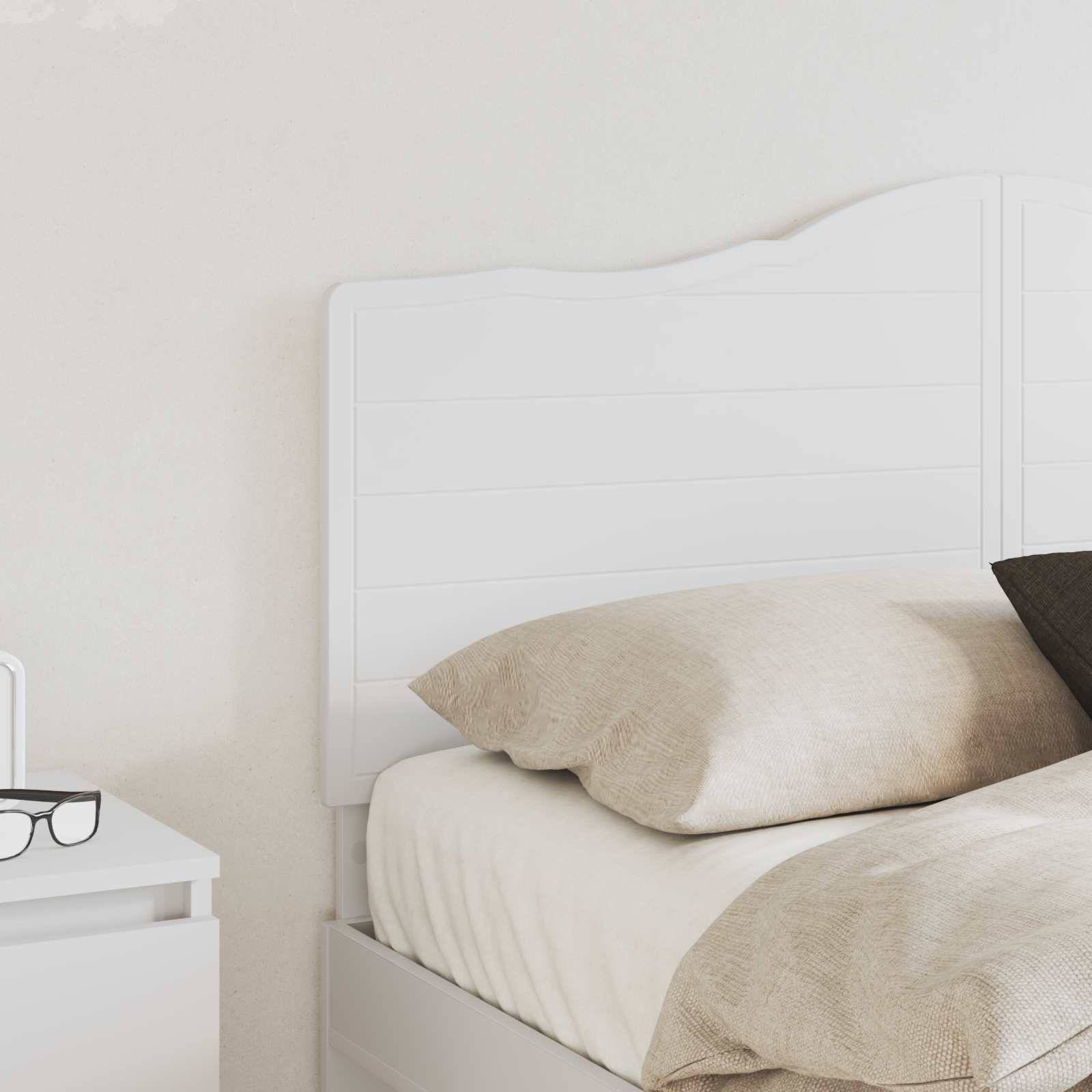 Ein ordentlich gemachtes weißes Bett mit beigefarbenen Kissen neben einem weißen Nachttisch, auf dem eine schwarzgerahmte Brille liegt.