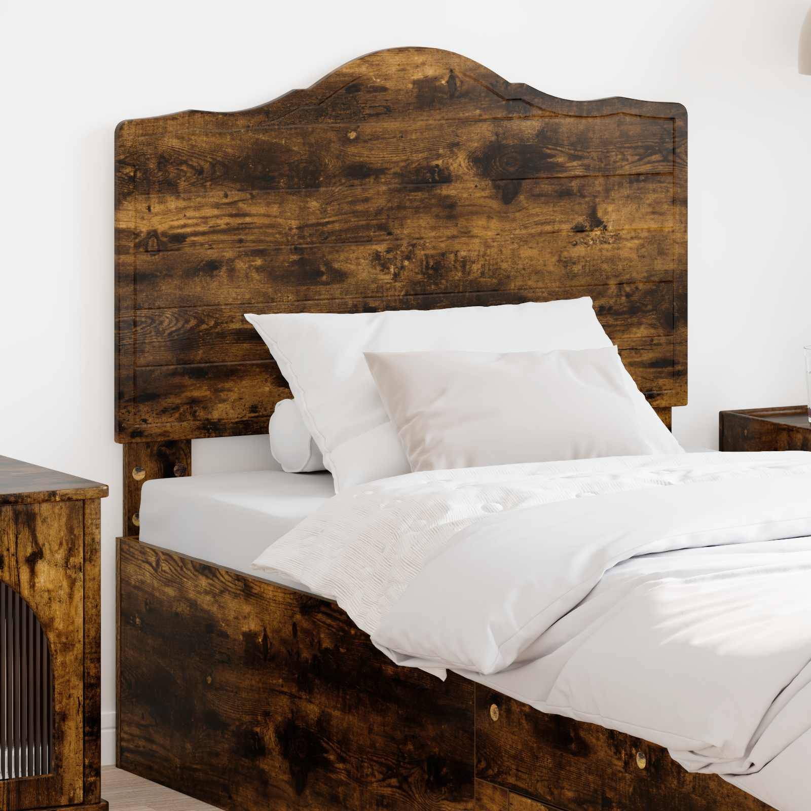 Ein Holzbett mit rustikalem Kopfteil und weißer Bettwäsche ist in einem hellen Raum zu sehen. Ein passendes Holznachttischchen ist teilweise sichtbar.