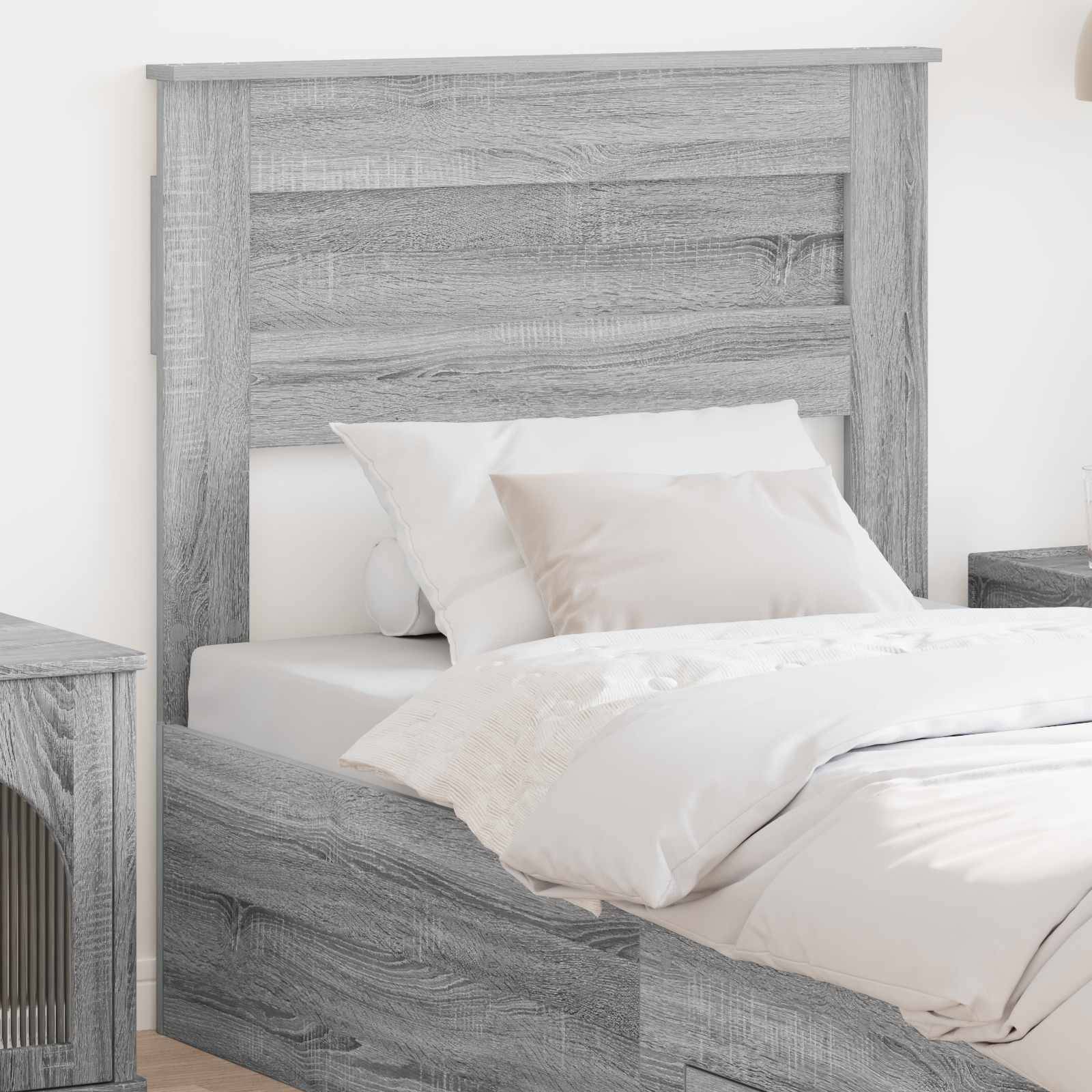 Ein hellgraues Holzbett mit hohem Kopfteil, weiße Bettwäsche und Kissen neben einem passenden Nachttisch in einer minimalistischen Raumgestaltung.