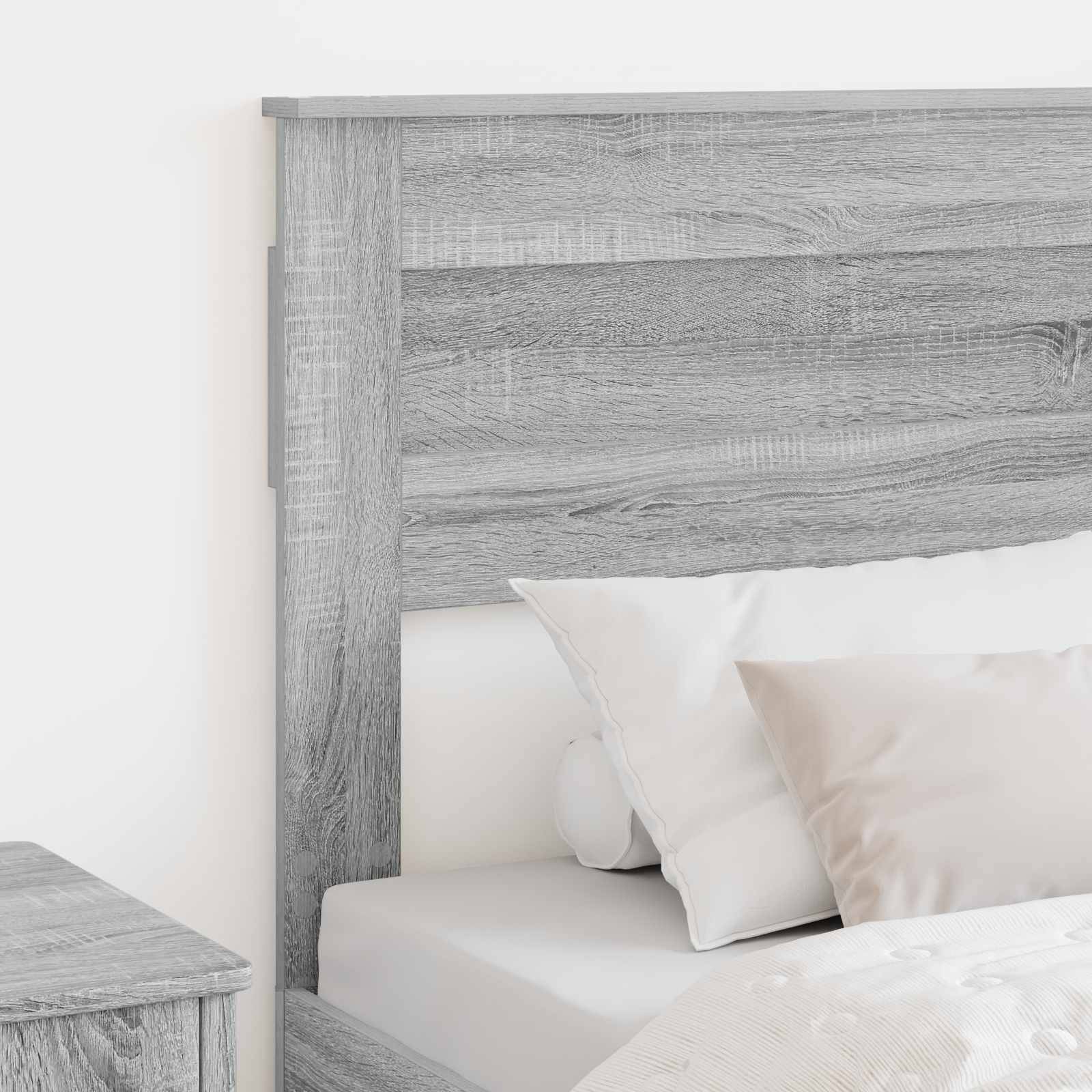Ein ordentlich gemachtes Bett mit weißen Kissen und einem hellgrauen Holzkopfteil sowie passendem Nachttisch, das eine ruhige Schlafzimmeratmosphäre schafft.