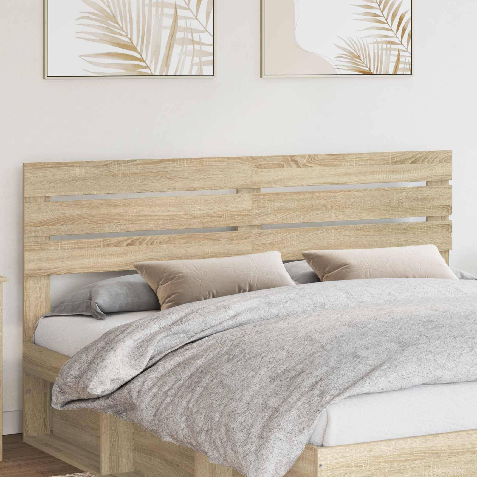 Ein ordentlich gemachtes Bett mit Holzrahmen und zwei neutral gefärbten Kissen vor einer Wand mit zwei abstrakten pflanzenthematischen Kunstwerken darüber.