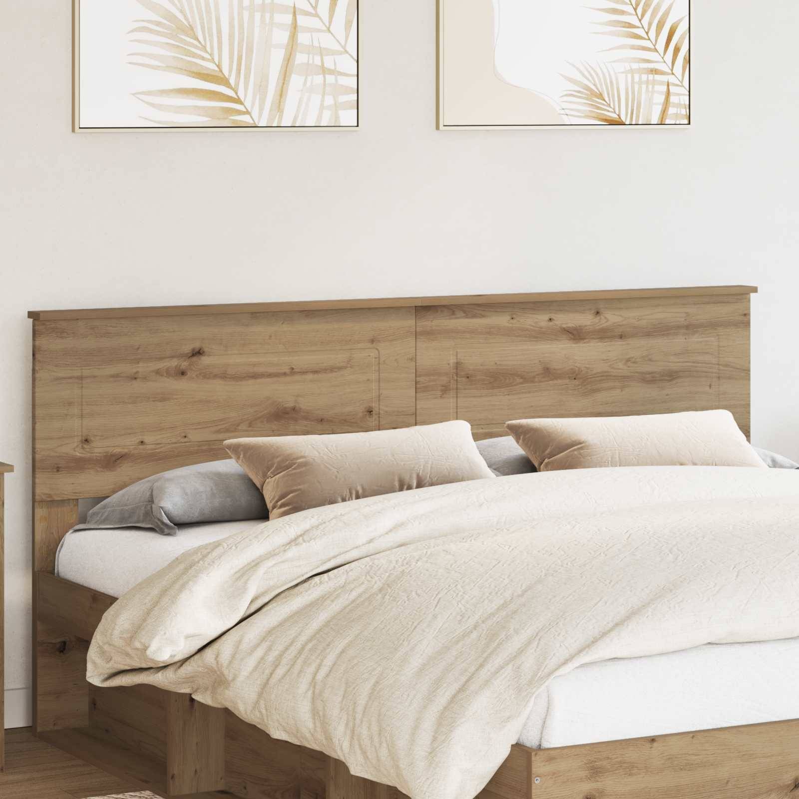 Ein ordentlich gemachtes Bett mit hellfarbiger Bettwäsche und Kissen, gerahmt von einem hölzernen Kopfteil. Zwei gerahmte Kunstwerke mit Palmblättern hängen darüber.