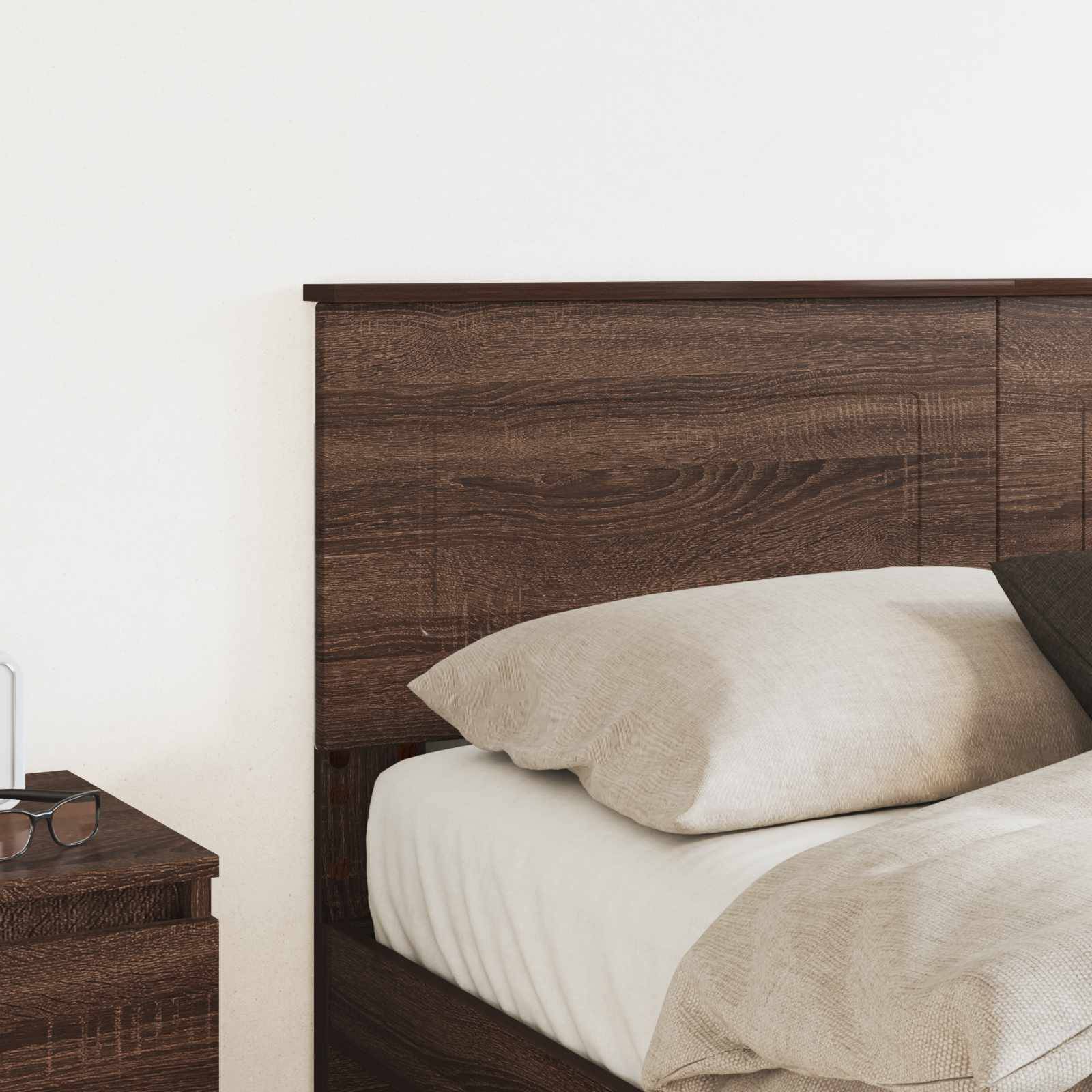 Ein ordentlich gemachtes Bett mit hölzernem Kopfteil und hellfarbigen Kissen sowie Decke; ein Nachttisch mit einem geschlossenen Buch daneben.