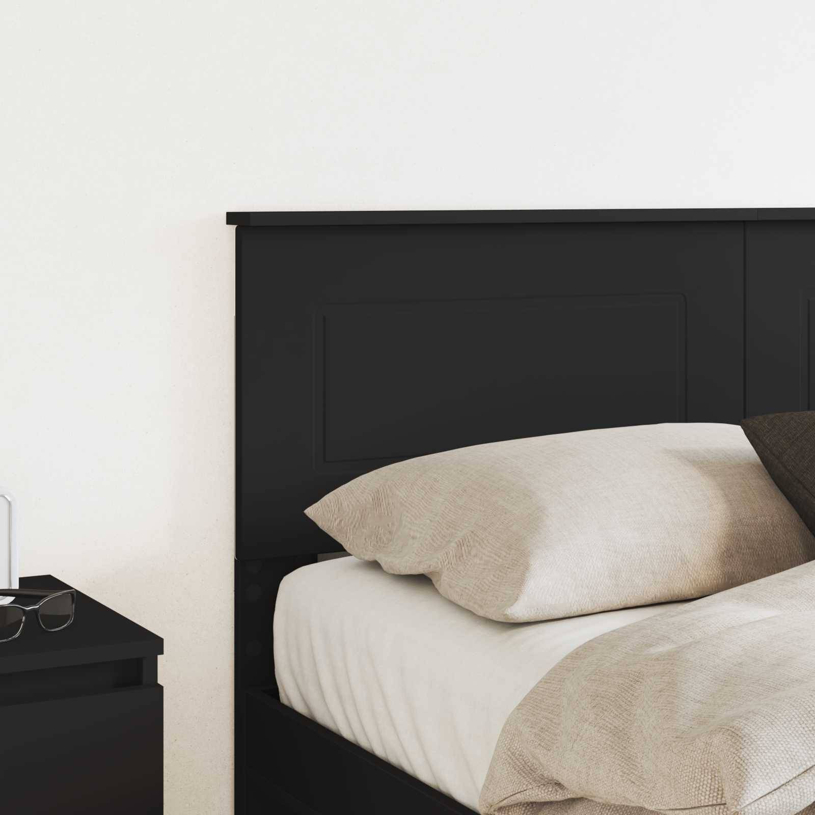 Ein ordentlich gemachtes Bett mit beigefarbener Bettwäsche und weißen Kissen ist vor einem schwarzen Kopfteil positioniert. Ein kleiner schwarzer Nachttisch ist teilweise sichtbar.