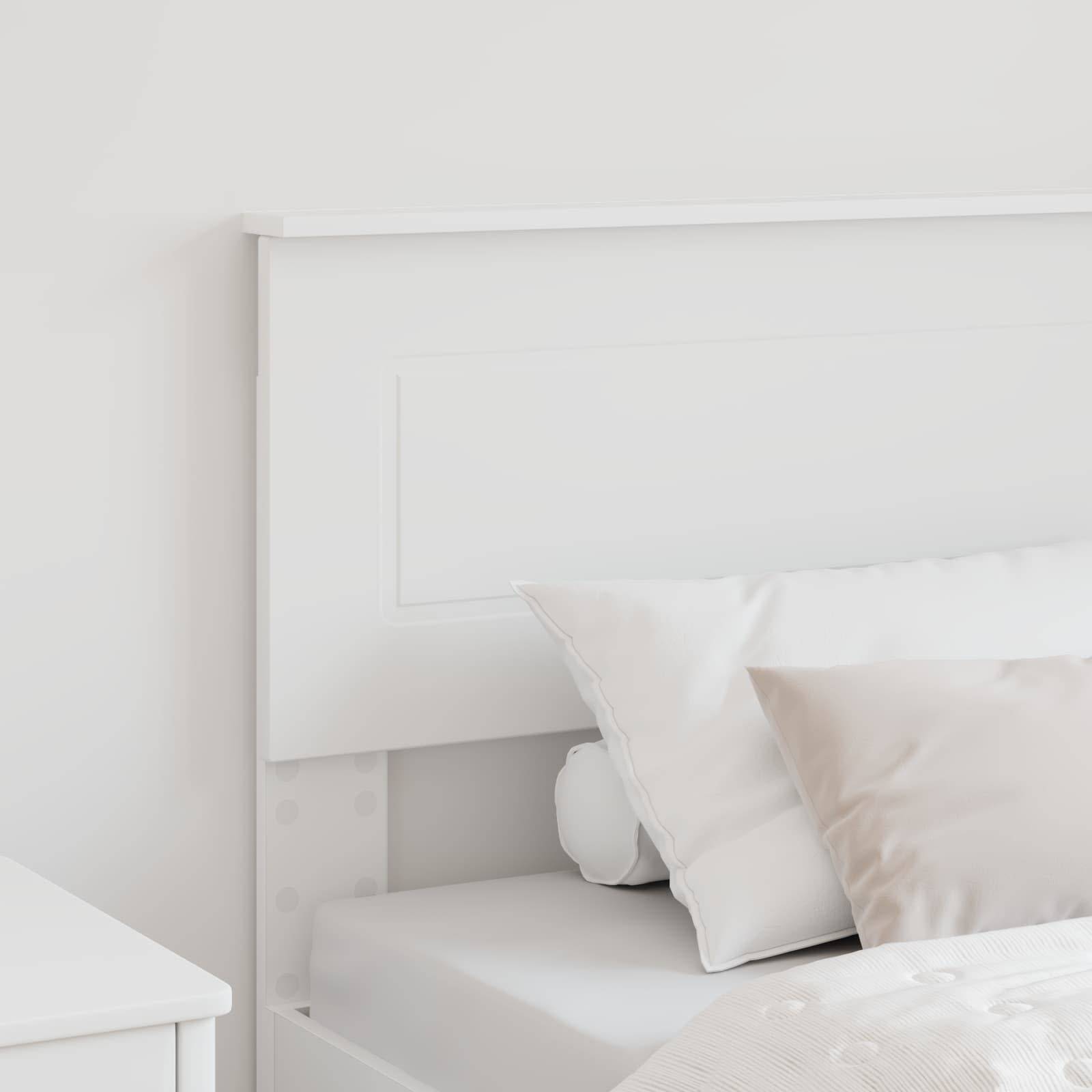 Ein ordentlich gemachtes Bett mit weißen Kissen und einer leichten Decke vor einem weißen Kopfteil in einem minimalistischen Schlafzimmer.