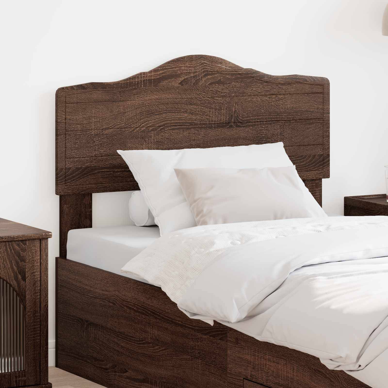 Ein Holzbett mit weißer Bettwäsche ist an einer hellfarbigen Wand aufgestellt. Neben dem Bett steht ein Holznachttisch.