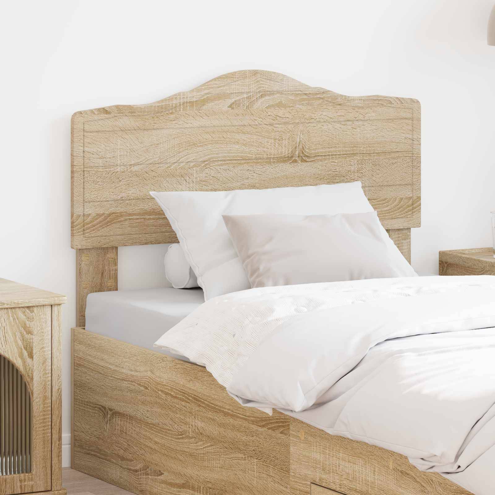 Ein ordentlich gemachtes Holzbett mit weißen Kissen und einer Daunendecke in einem hellen Zimmer. Ein kleines hölzernes Nachttischchen ist auf der linken Seite positioniert.
