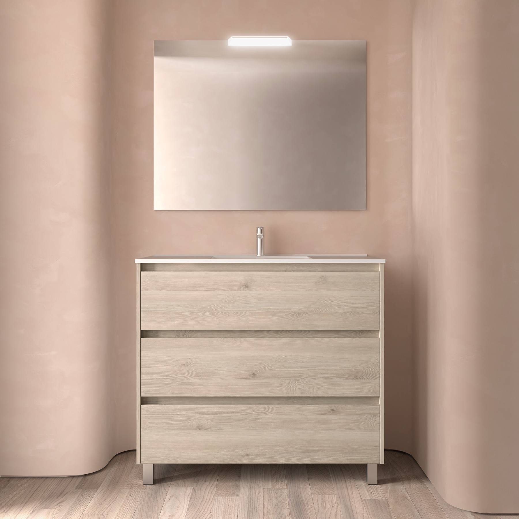 Waschtisch aus Holz mit drei Schubladen, gekrönt von einem Waschbecken und Wasserhahn, vor einer rosafarbenen Wand mit einem großen Spiegel und einer Deckenlampe.