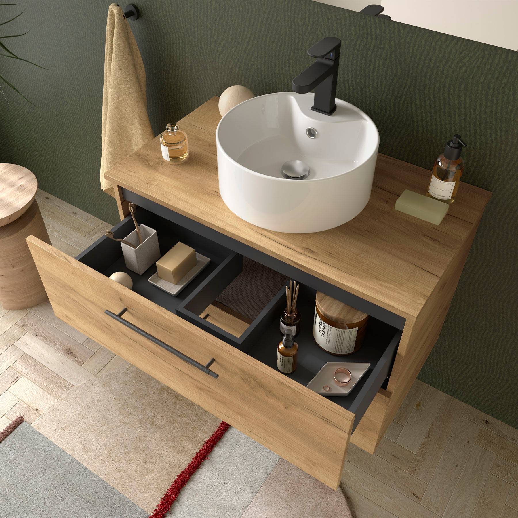 Holz-Badezimmerschrank mit geöffneter Schublade, in der Toilettenartikel zu sehen sind. Rundes weißes Waschbecken und schwarzer Wasserhahn oben, dazu ein Handtuch und Seife.