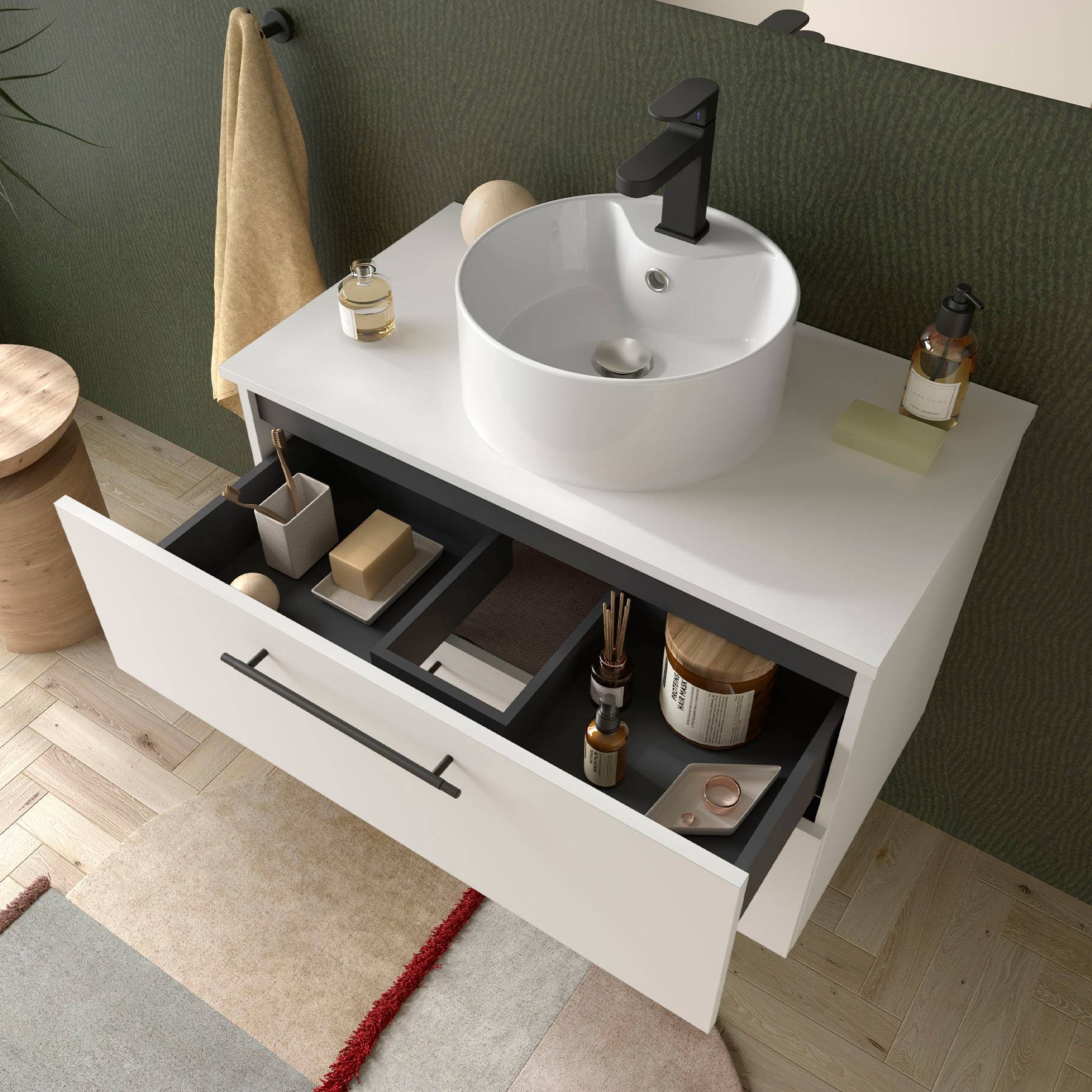 Badezimmerwaschtisch mit einer offenen Schublade darunter, die ordentlich angeordnete Toilettenartikel und einen Zahnbürstenhalter zeigt; grüner strukturierter Wandhintergrund.