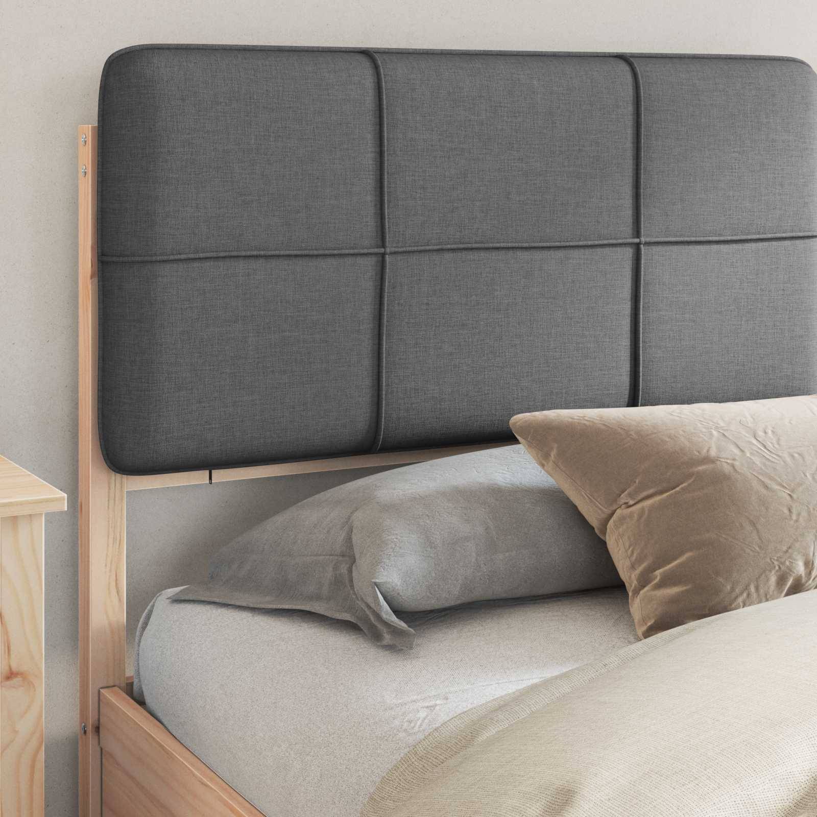 Ein grau gepolsterter Kopfteil mit Knopfheftung ist an einem Holzbettgestell befestigt. Das Bett ist mit grauen und beigen Kissen bezogen.