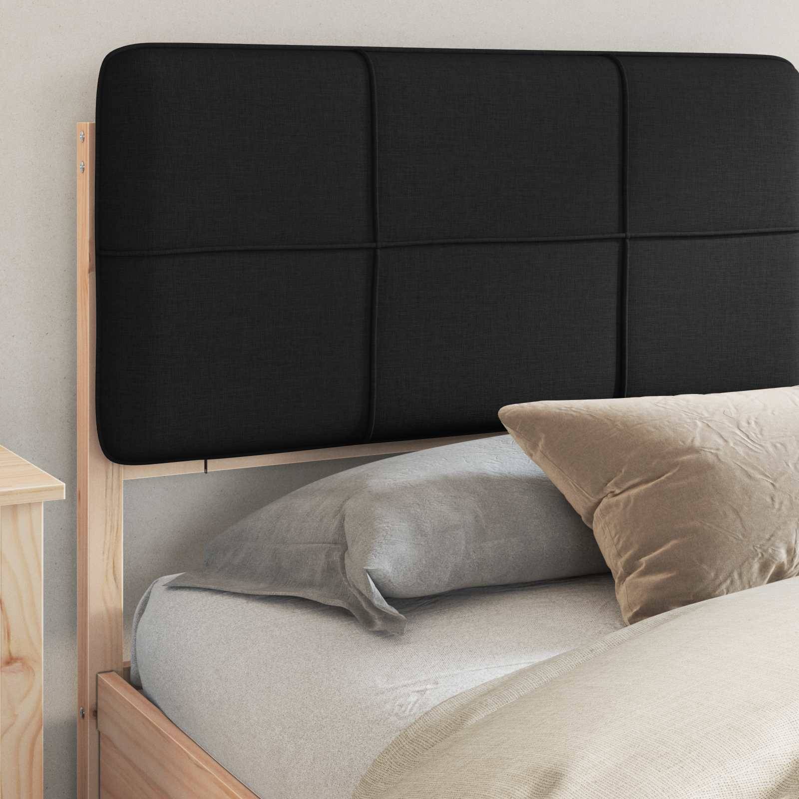 Ein ordentlich gemachtes Bett mit einer hellgrauen Steppdecke und einem beigen Kissen vor einem schwarzen gepolsterten Kopfteil. Der Bettrahmen ist aus hellem Holz.
