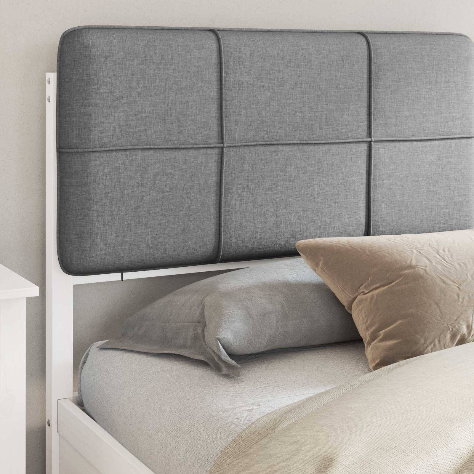 Ein sauber gemachtes Bett mit einem grauen gepolsterten Kopfteil, beigen Kissen und einem weißen Nachttisch. Die Hintergrundwand ist hellfarben.