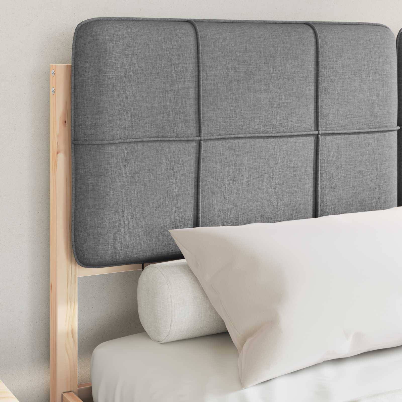 Ein Holzbett mit einem grauen gepolsterten Kopfteil und weißer Bettwäsche wird gezeigt, das einen zylindrischen weißen Kissen enthält.