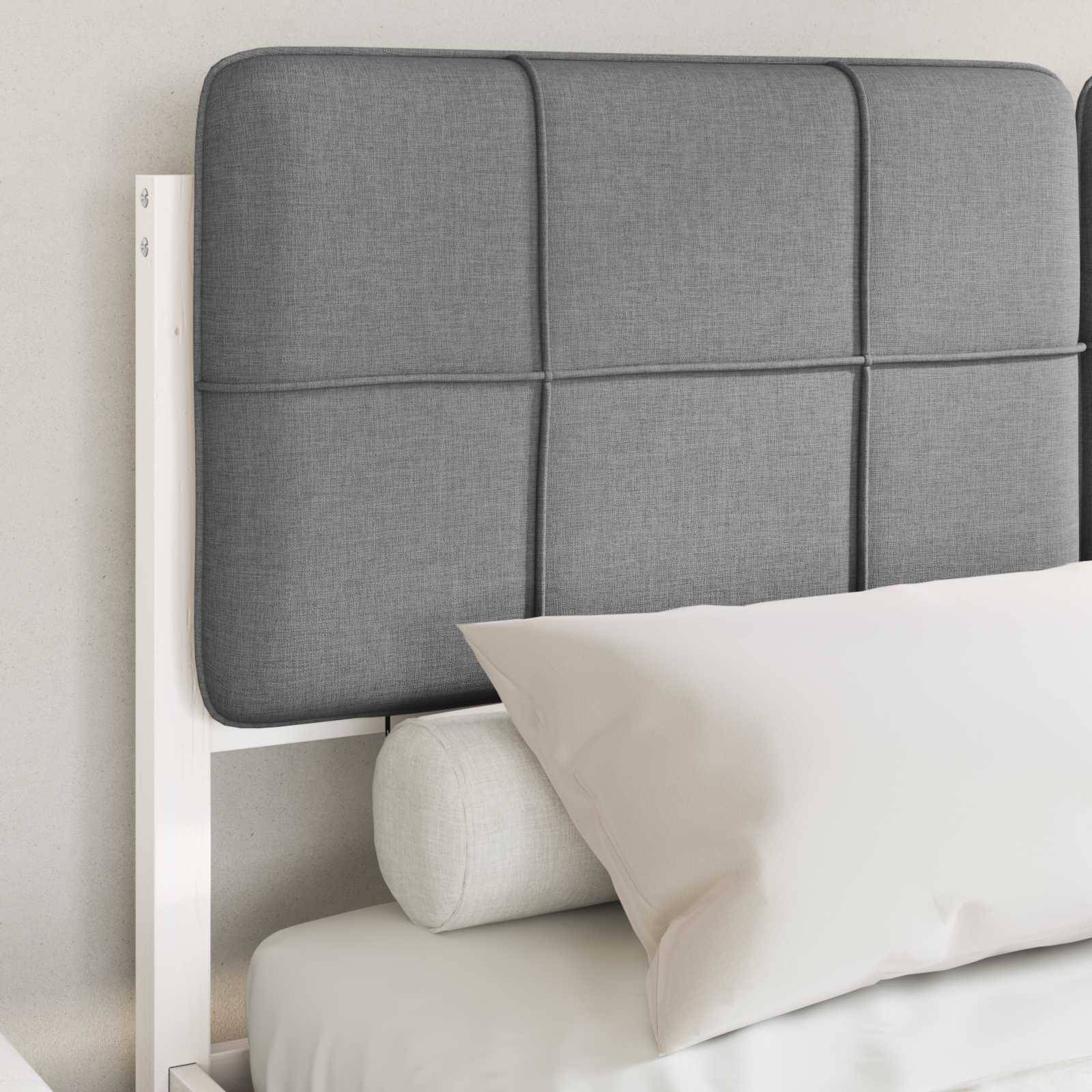 Ein grau gepolsterter Kopfteil mit horizontalen und vertikalen Steppnähten ist an einem Bett mit weißer Bettwäsche und einem zylindrischen Kissen befestigt.