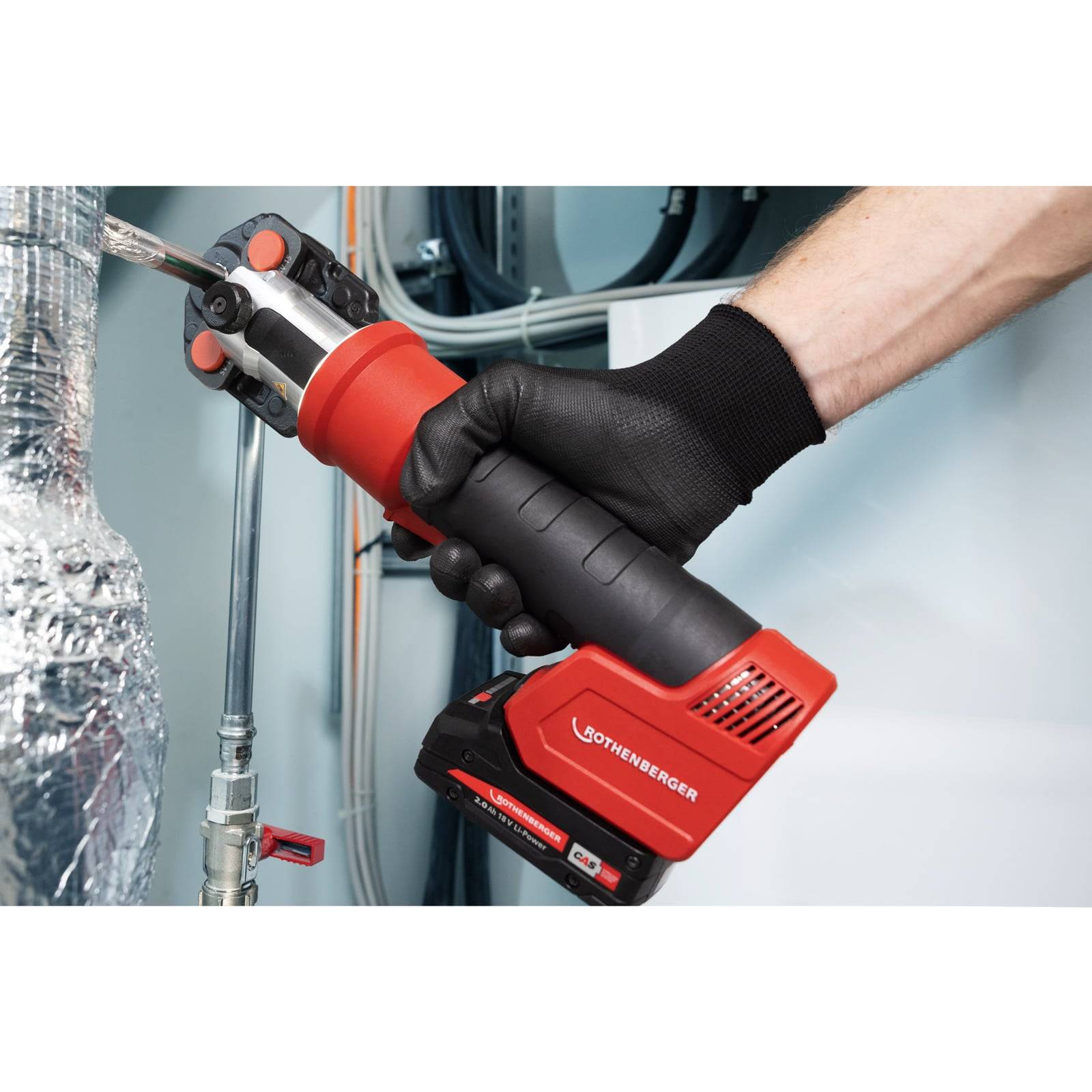 Eine Person mit einem schwarzen Handschuh verwendet ein rotes und schwarzes ROTHEBERGER-Werkzeug auf einer Metalloberfläche, möglicherweise zum Schneiden oder Reparieren von Rohren.