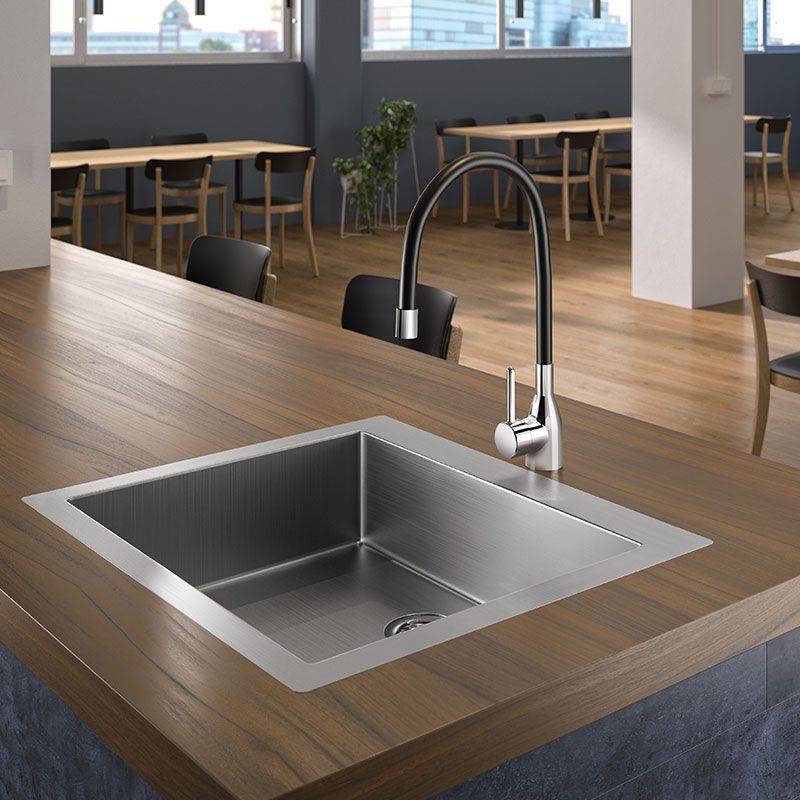 Moderne Küche mit einer Holzarbeitsplatte, Edelstahlspüle und elegantem Wasserhahn. Im Hintergrund befinden sich Tische, Stühle und große Fenster.