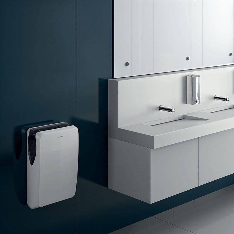 Modernes Badezimmer mit zwei weißen Waschbecken, wandmontiertem Seifenspender, eleganten Armaturen und einem Händetrockner an der dunklen Wand.