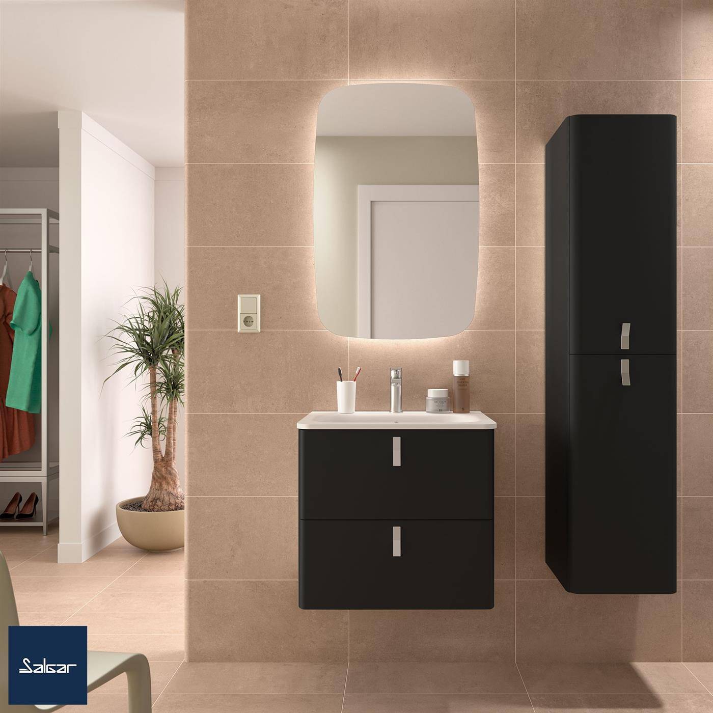 Modernes Badezimmer mit beigen Fliesenm­auern, wandmontiertem Waschbecken und Spiegel, schwarzen Schränken und einer hohen Aufbewahrungseinheit neben einem offenen Kleiderschrank und einer Topfpflanze.